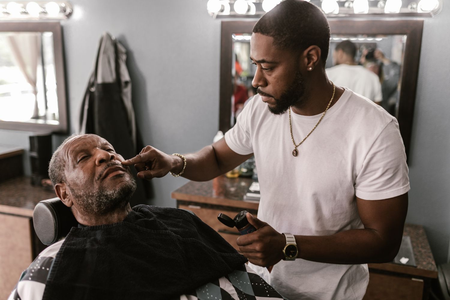 A barber sculpting and detailing an older client's beard with precision