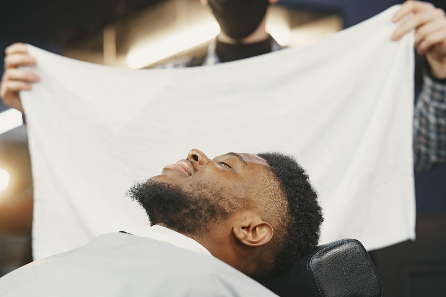 A client reclined in the chair with a warm towel draped over his face during the hot towel service