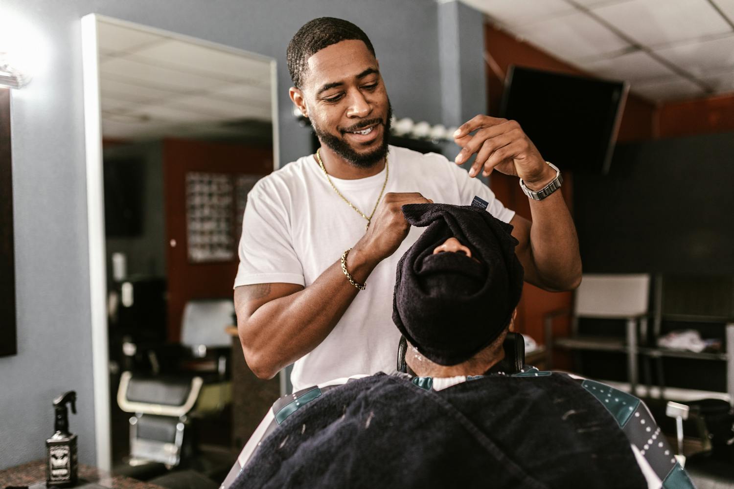 A barber wrapping a warm towel around a client's head, smiling, in the shop